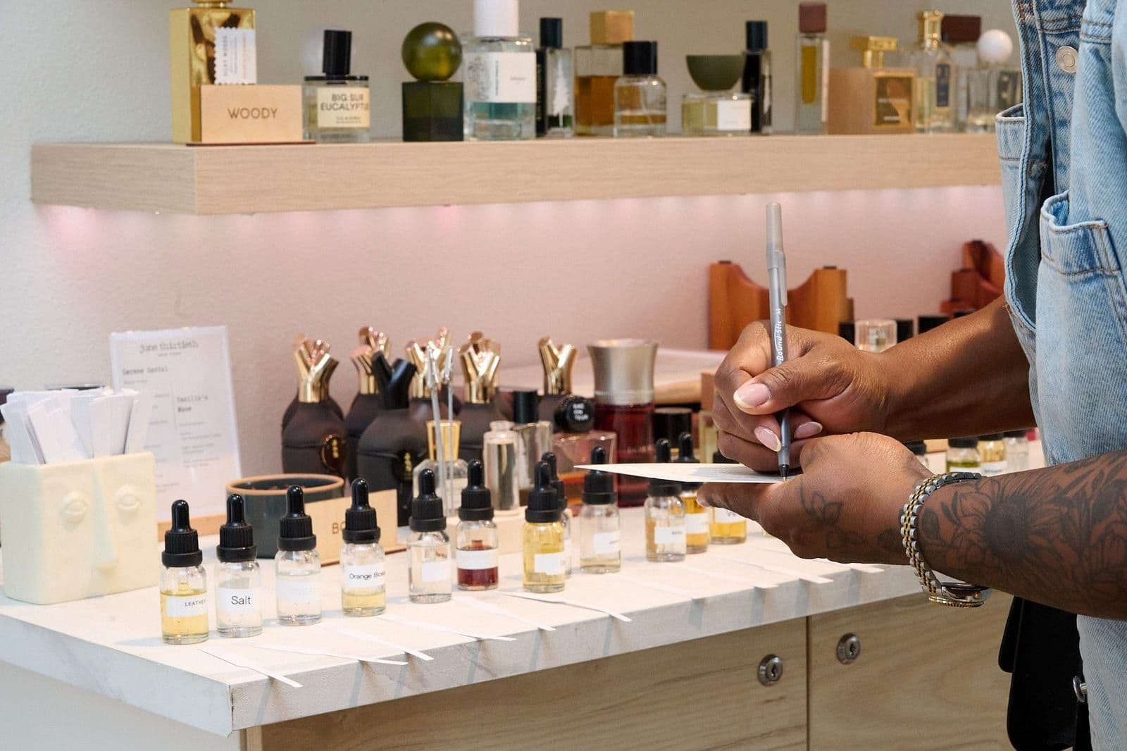 A guest writing her formula notes beside labelled bottles of leather, salt and orange blossom